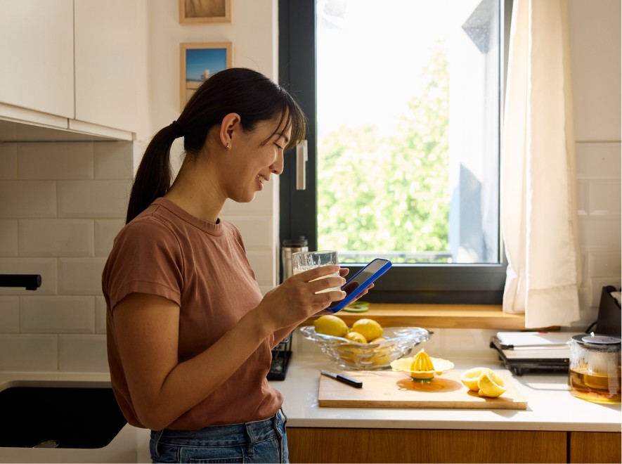 A young smiling female looking at her phone in a kitchen during breakfast