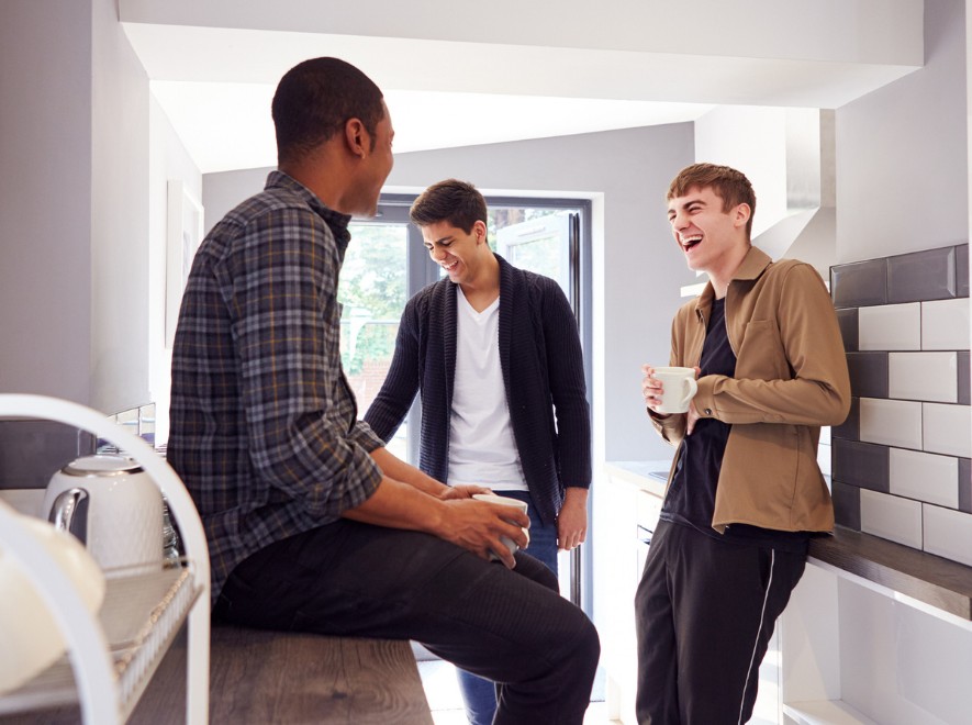 young male students smiling while socializing in a kitchen